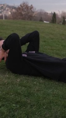 Genç adam parkta egzersiz yapıyor, çimlerin üzerinde egzersiz yapıyor, vücudunu korumak için çimlerin üzerinde mekik çekiyor.