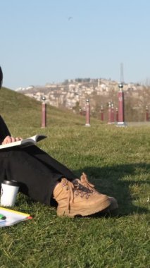 Genç, güzel bir kadın çimenler üzerinde kitap okumaktan, güneşli bir pazar günü açık hava aktivitesinden, temiz hava ile ilgili bir kitapla ilgilenmekten hoşlanıyor.