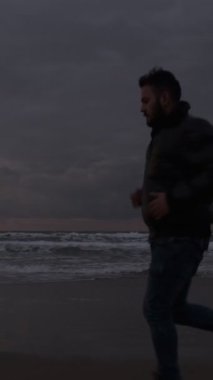 Spor yapan bir adamın, dalgalarla yarışır gibi, plajda rahatlama seansı yaparken görüntüsü.