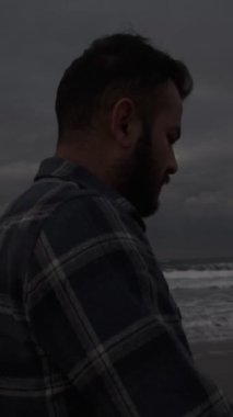 Genç adam sahildeki muhteşem manzarayı seyrediyor. Yürüyüş stili sakin. Sahilde yürüyen insanları görüyor.