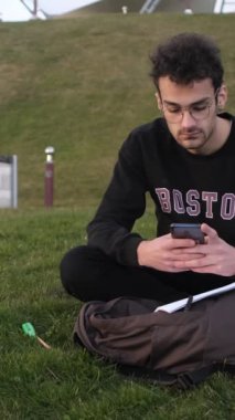 Temalı bir resimde, genç adam telefonuyla parkta tek başına mesajlaşırken, dışarıda çalışırken önündeki gazete ve telefonları hallederken, yaz tatilinde düşünmek için dinlenirken görülüyor.