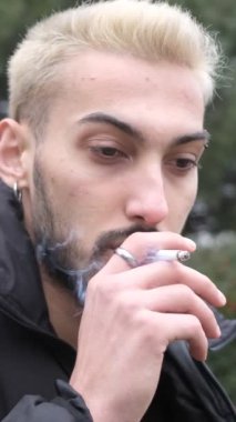 Parkta sigara içen genç bir adamın görüntüsü, gözlerini kaçırmayı düşünen genç bir adamın, sonbaharda parkta vakit geçirmesi.