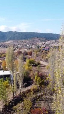 Sonbaharda köyün havadan görünüşü, kırsaldaki ev ve bahçelerin manzarası, dağlar ve ağaçların arasından gökyüzü.