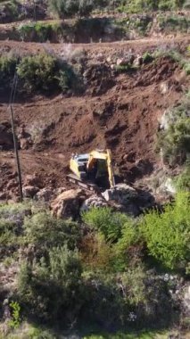 Vadideki çalışma makinesinin ve çevresindeki tarım alanlarının hava görüntüsü, kazıcı toprak bir yolun önündeki büyük taşları çekiyor.