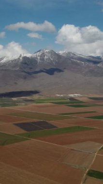 Hava manzarası ve dağ manzarası bulutlu ve berrak bir gökyüzü altında, yan yana ekilmiş bir sürü tarım arazisi.