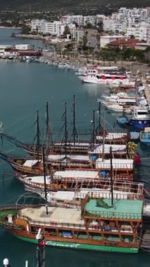 Marinada demirlemiş teknelerin hava aracı görüntüsü, teknelerin ve şehir manzarasının yukarısı, turkuaz sularda duruyor.