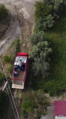 Sera işçileri topladıkları ürünleri kamyona yükledi ve kamyon ayrılıyor. Evlerin ve seraların içinden geçen kamyonun havadan görüntüsü.