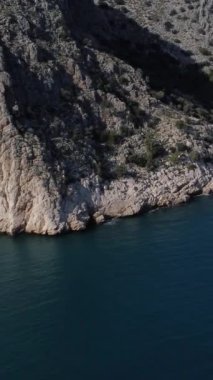 Denizin hemen ucunda uzanan dağlar bir uçurum oluşturur, dalgaların vurduğu sahilin havadan görünüşü, güzel mavi suların manzarası.