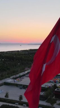 Milli bayrak sallayan hindiler, parka dikilen bayrağın havadan görünüşü, akşam şehir manzarası, denize yansıyan gün batımı