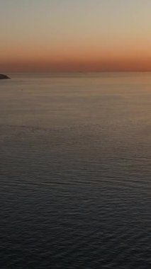 Deniz batımı adasının havadan görünüşü, rengarenk günbatımının drone görüntüsü ve denizde bir tekne, denizin ortasında bir kara parçası.