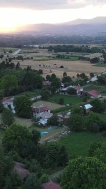 Yeşil ağaçların arasına inşa edilmiş köy ve köy yolunun hava manzarası. Bir şerit kasaba yolundan geçen bir araba.