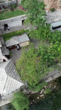 Vrelo Bune şehrinin dağ altındaki hava aracı görüntüsü, kayanın altına ve Bosna-Hersek 'teki Buna nehrinin kıyısına inşa edilmiş tarihi derviş kulübesi