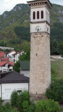 Şehirdeki evler arasındaki tarihi binanın önündeki saat kulesinin insansız hava aracı görüntüsü, Bosna 'daki evler arasındaki kültür mirası