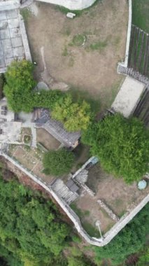 Tarihsel ortaçağ şatosunun insansız hava aracı görüntüsü, dağ ayağına tünemiş antik taş kale manzarası, surlar ve ormandaki gözetleme kuleleriyle çevrili yapı.