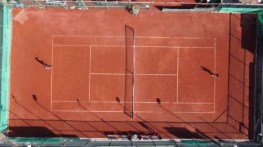 Sahada tenis oynayan iki adamın yukarıdan çekimleri, tenis oynayan gençler eşyalarını kortun kenarına koydular.
