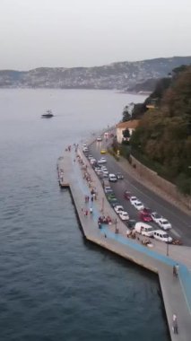 İnsansız hava aracı kıyı şeridinde yürüyor, insanlar akşamları deniz kenarında yürüyor, denizden geçen yatların havadan görünüşü...