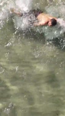 İnsansız hava aracı görüntüsü, açık okyanus denizinde parlak siyah şortlu bir adam, kristal berraklığında turkuaz dalgaların arkasını görüyor, rahat ve serin bir tatil hak ediyor. 