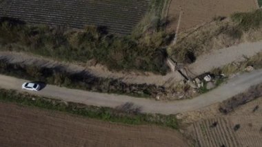 Vadi ile toprak yol arasındaki tarım arazisi ve toprak yolda giden arabanın hava manzarası, ekili arazili yan bahçeler.