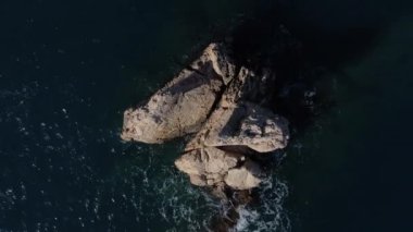 Kayalık adanın üzerinde yükselen tepeden bakan manzara, adanın üzerinde yükselen insansız hava aracı manzarası, mavi suların ortasında yükselen büyük kayanın manzarası.