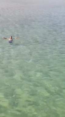 İnsansız hava aracı görüntüsü, açık okyanus denizinde parlak siyah şortlu bir adam, kristal berraklığında turkuaz dalgaların arkasını görüyor, rahat ve serin bir tatil hak ediyor.