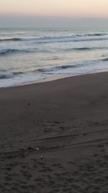 Sabahları deniz kenarında güneş ışığına karşı kamp çadırı. Sahilde ateşin yanında oturan iki adam.