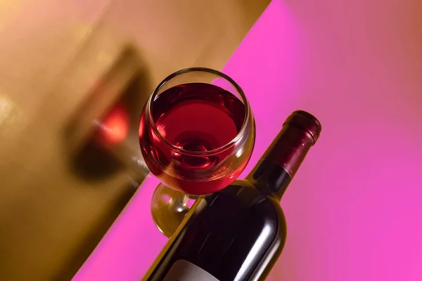 Glass and bottle of red wine on a pink abstract background.