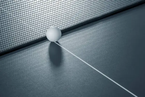 A ball for playing table tennis on a table against a background of a net.
