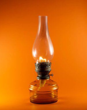 Turuncu arka planda cam bir şişede yanan eski bir gaz lambası..