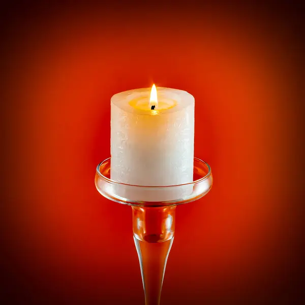 Kırmızı arka plandaki cam tezgahta yanan mum..
