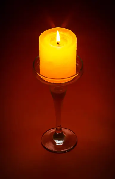 Kırmızı arka plandaki cam tezgahta yanan mum..