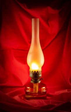 Kırmızı buruşuk kumaştan bir arka planda paslı, yanan bir gaz lambası..