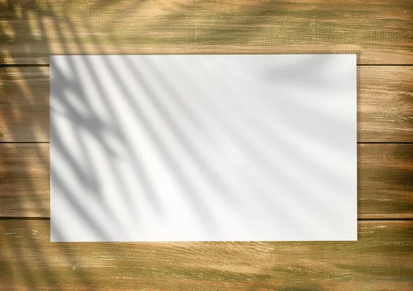 Empty white list on an old style wooden empty background with plam leaf shadow on it. Empty paper mockup, top view