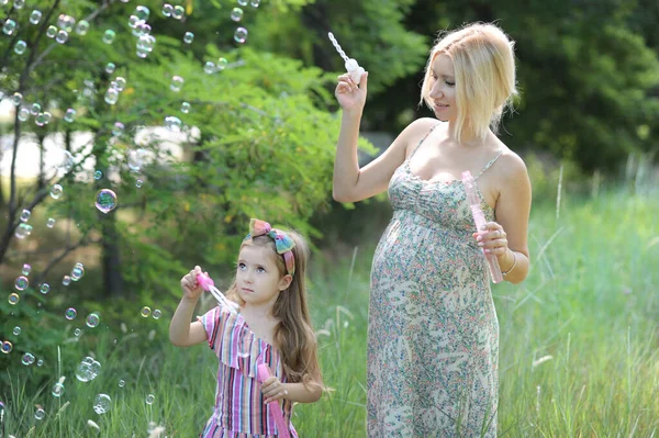 小女孩和她怀孕的妈妈在公园外面吹泡泡很开心 — 图库照片