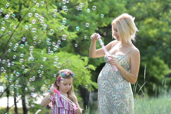 小女孩和她怀孕的妈妈在户外吹泡泡很开心 — 图库照片