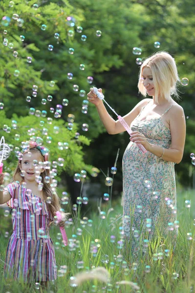 小女孩和她怀孕的妈妈在公园里玩乐地吹泡泡 — 图库照片