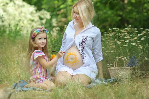小女孩在怀孕妈妈的肚子上画太阳 在公园的外面 — 图库照片