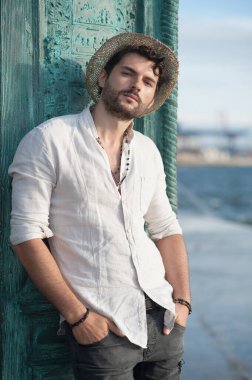 Büyük şehirde deniz kenarında şapka takmış yakışıklı bir adam.