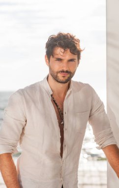 Beyaz gömlekli yakışıklı bir adam, deniz manzaralı bir açık hava portresi.