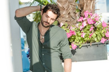 Yeşil gömlekli yakışıklı adam, tropikal şehir manzarasına karşı açık hava fotoğrafı.