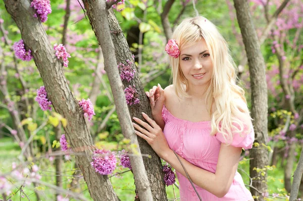 可愛いピンクのドレスを着て 春の開花公園でポーズをとっているかなり幸せなブロンドの女性 — ストック写真