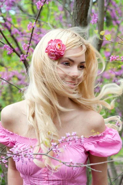 漂亮而快乐的金发蓬松的女人 穿着漂亮的粉色连衣裙 在春花公园里摆姿势 — 图库照片