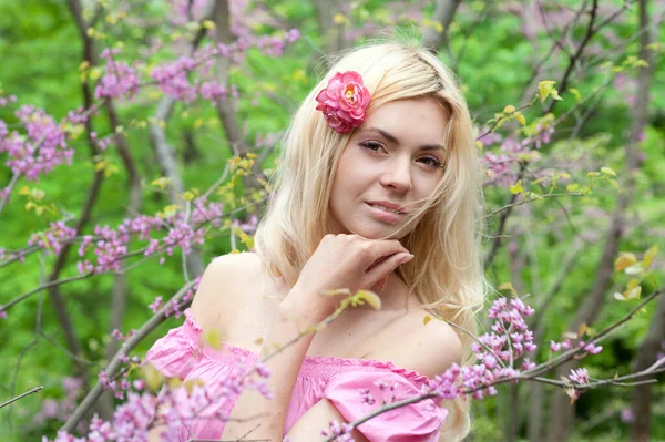 ピンクの花の春の公園に身を包んだかわいいピンクのドレスを着た若い美しい女性 — ストック写真