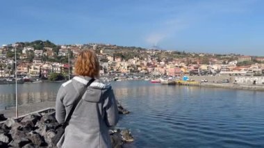 Tourist woman takes pictures with a smartphone of the sea and volcano. Woman looking at the sea and volcano Etna in Sicily, Acitrezza