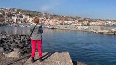 Tourist woman takes pictures with a smartphone of the sea and volcano. Woman looking at the sea and volcano Etna in Sicily, Acitrezza