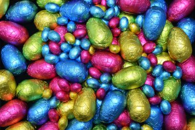 Pile or group of multi colored and different sizes of colourful foil wrapped chocolate easter eggs in pink, blue, yellow and lime green. 