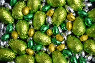 Büyük sarı, altın, yeşil, ıhlamur yeşili ve gümüş bahar renklerinde folyoya sarılı paskalya yumurtaları, siyah arka planda.