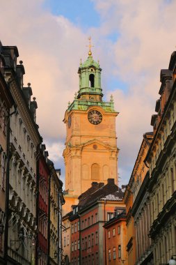 Clock tower of the Church of St Nicholas, behind a historic street of colourful buildings in the old town Gamla Stan, Stockholm, Sweden. 