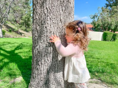 Şirin küçük kız parkta çimlerin ve ağaçların etrafında oynuyor.