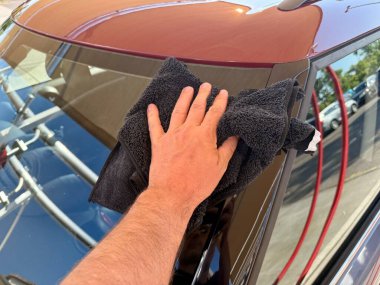 Araba yıkama yerinde siyah mikrofiber bezle el temizliği yapan bir adam var.