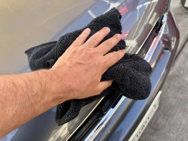 Araba yıkama yerinde siyah mikrofiber bezle el temizliği yapan bir adam var.